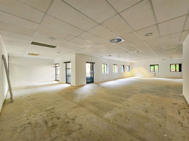 Spacious open-plan office area featuring a suspended ceiling, recessed lighting, air conditioning vents, and large windows, currently in a shell condition.
