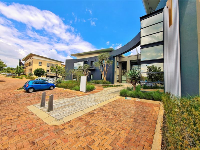 Modern office building exterior featuring contemporary architectural design, glass curtain walls, metal cladding, and a well-maintained paved entrance area with landscaped surroundings.