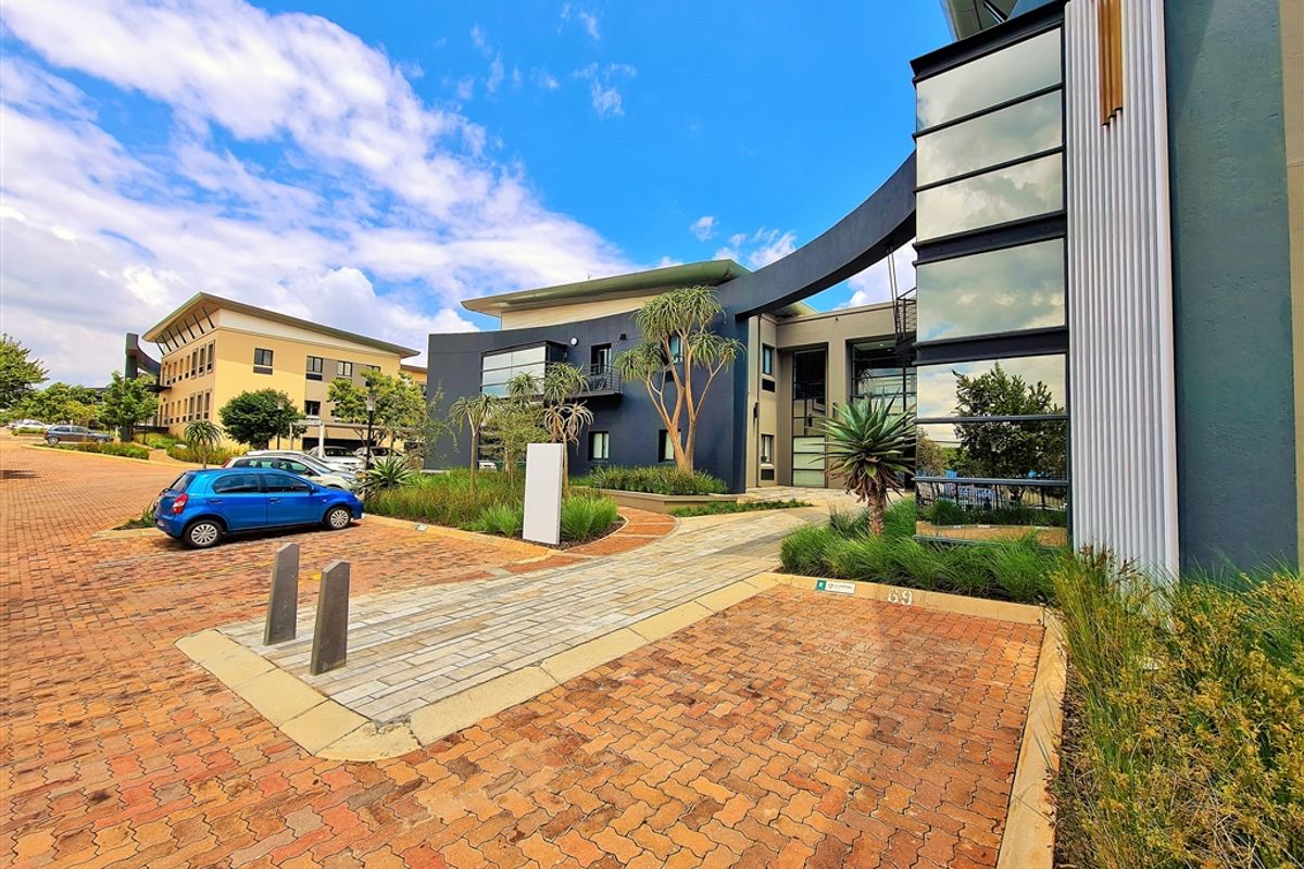 Modern office building exterior featuring contemporary architectural design, glass curtain walls, metal cladding, and a well-maintained paved entrance area with landscaped surroundings.