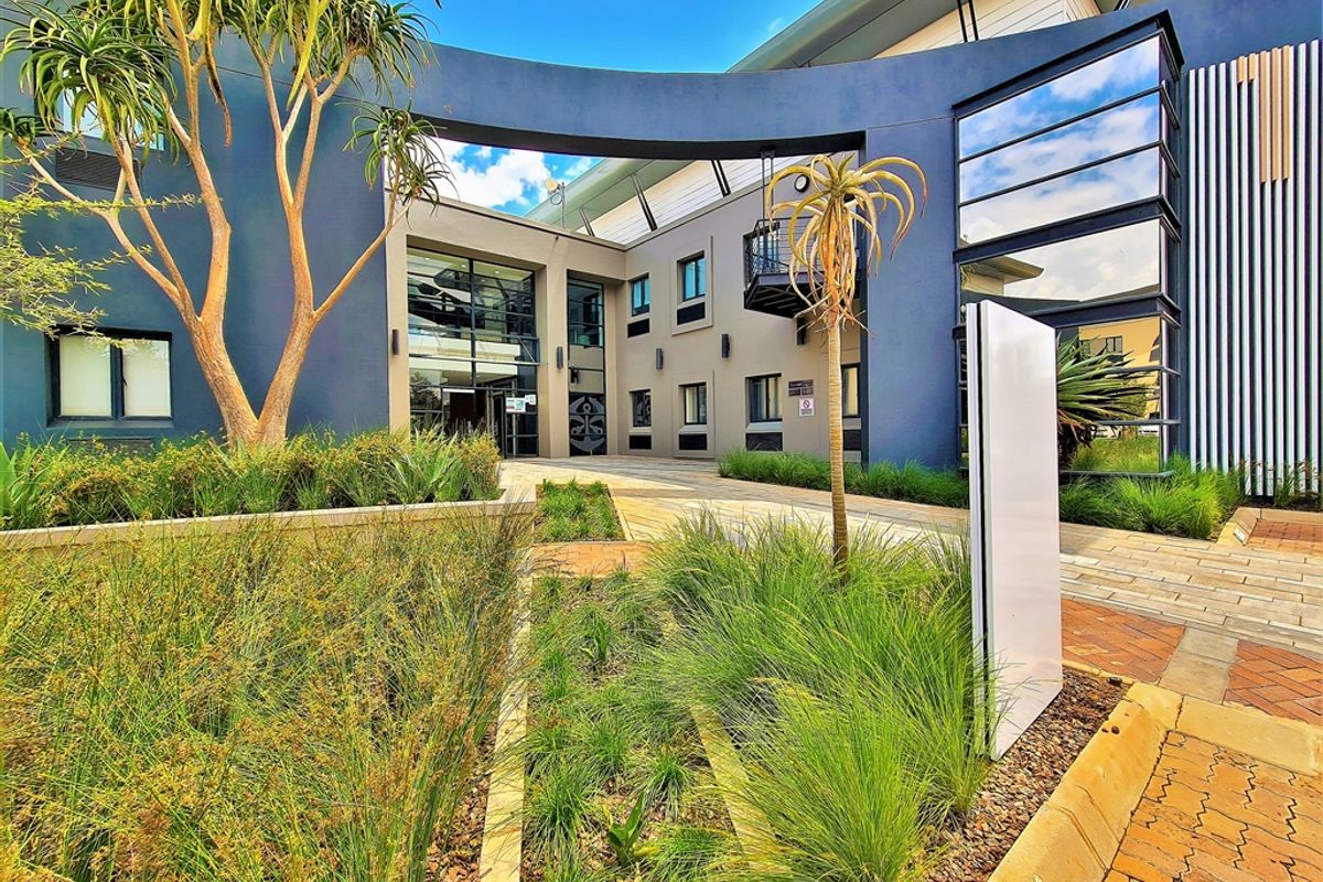 Modern office building entrance featuring contemporary architectural design, glass facade elements, and well-maintained landscaped garden beds with a paved approach.