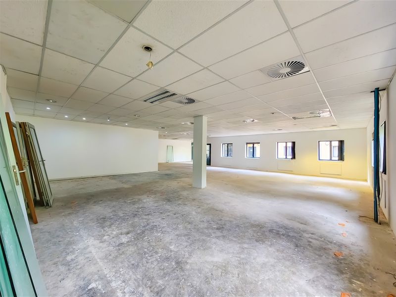 A large, open-plan office space featuring a suspended ceiling, structural support column, and multiple windows, currently in a shell condition ready for fit-out.