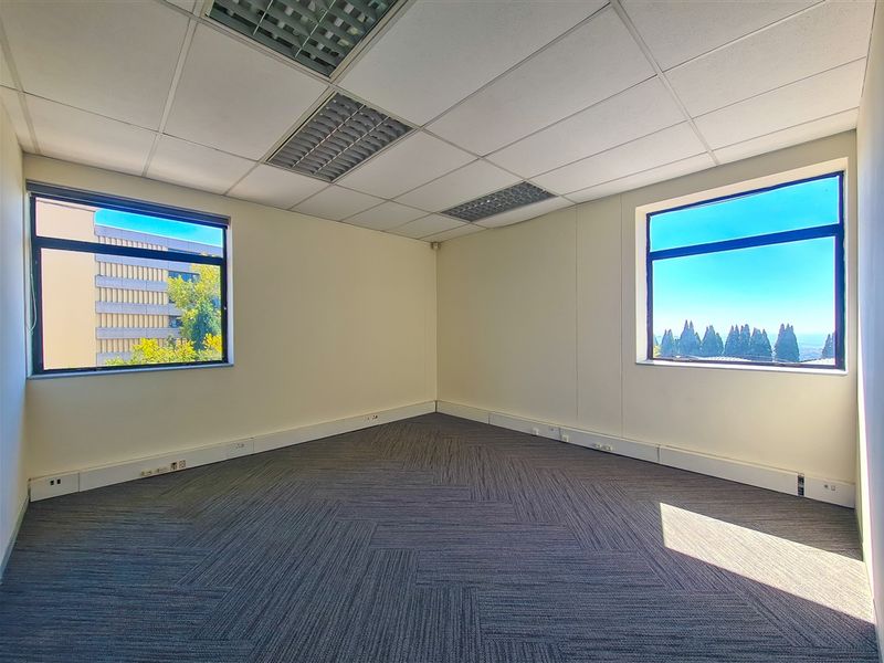 A bright, empty office space featuring carpet tiles, suspended ceilings with recessed lighting, and perimeter trunking for electrical connectivity, offering pleasant exterior views.