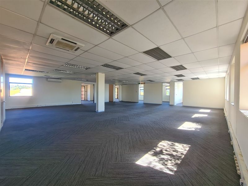 A spacious, open-plan office area featuring a suspended ceiling with recessed lighting, carpeted flooring, and integrated air conditioning units.