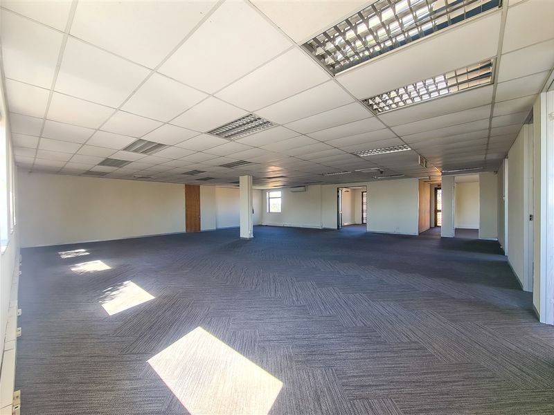 A spacious, open-plan office area featuring a suspended ceiling with recessed lighting, carpeted flooring, and a central support column.