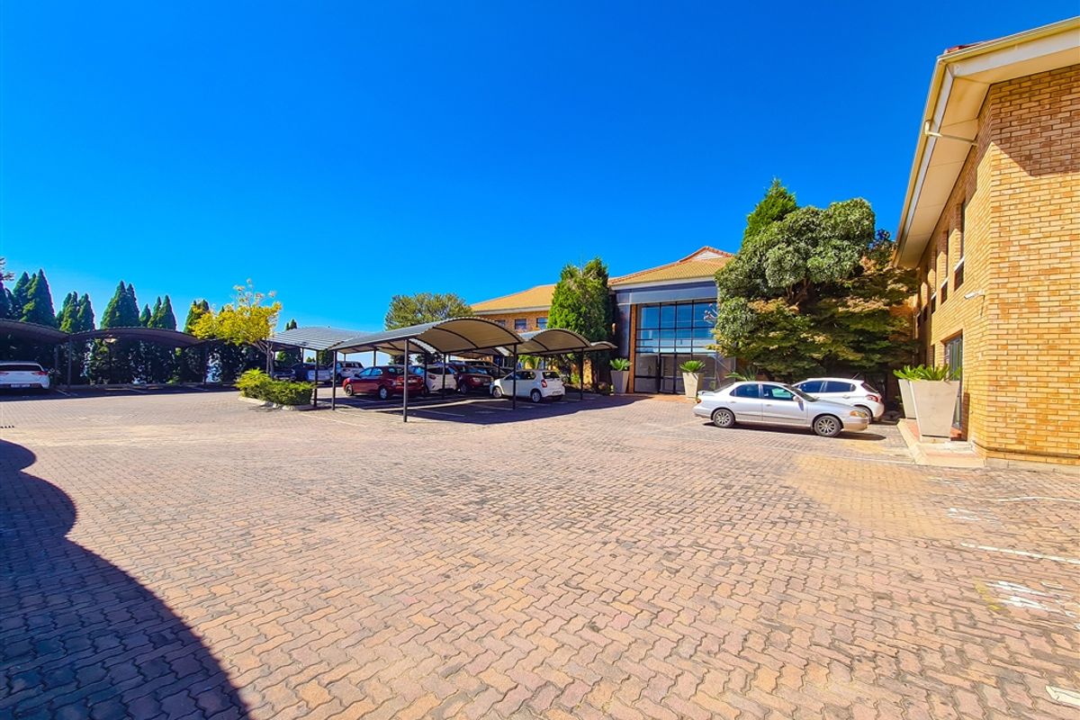 Exterior view of the office building featuring a large paved parking area with covered carports and a prominent glass entrance facade.