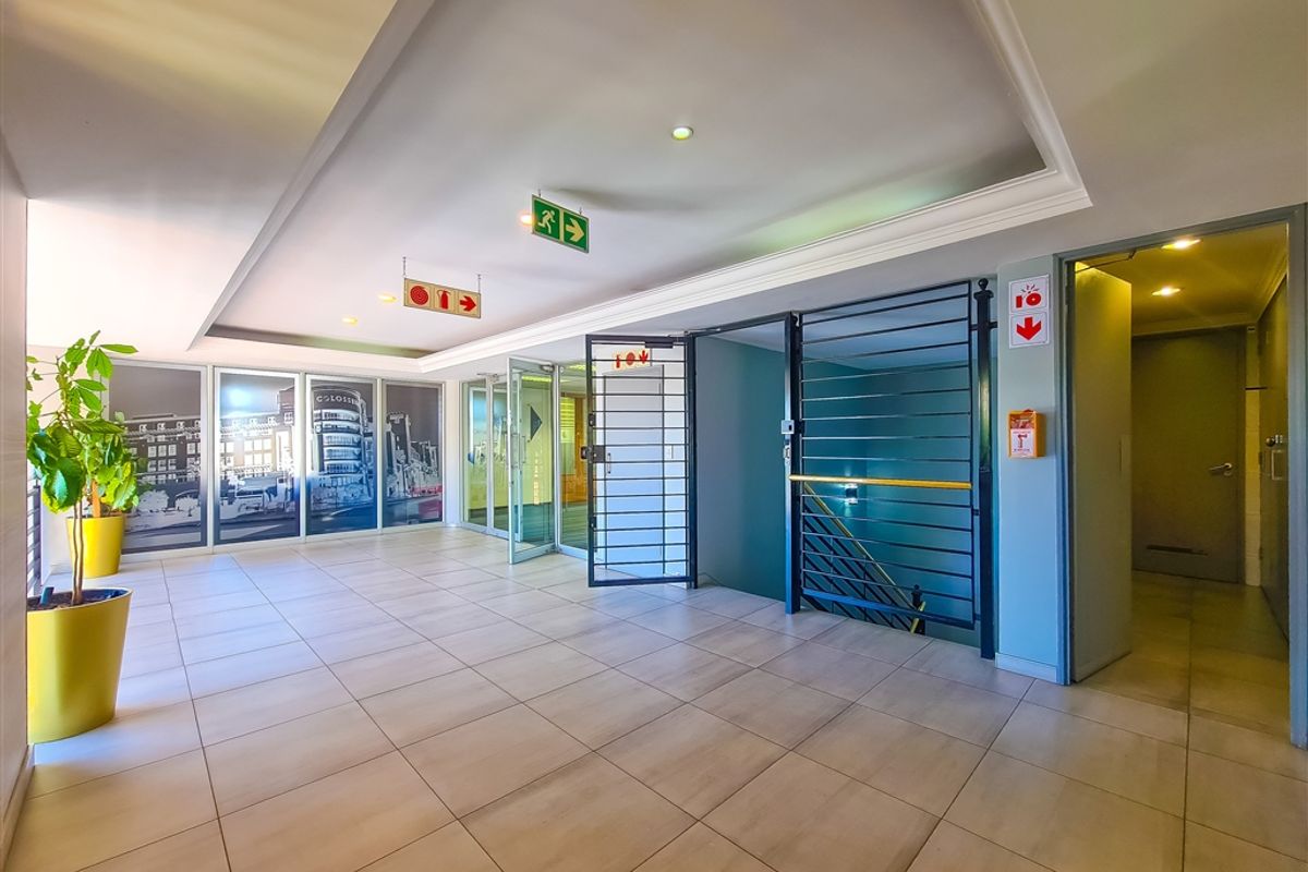 A well-maintained office building hallway featuring tiled flooring, recessed ceiling lighting, and secure access points with integrated fire safety equipment.