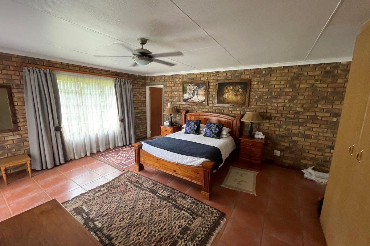 Spacious bedroom featuring exposed brick walls, tiled flooring, and a ceiling fan, offering a rustic and comfortable atmosphere.