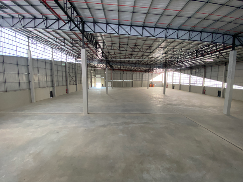 A large, open-plan industrial warehouse space featuring high ceilings with exposed steel trusses, concrete flooring, and ample natural light through translucent wall panels.