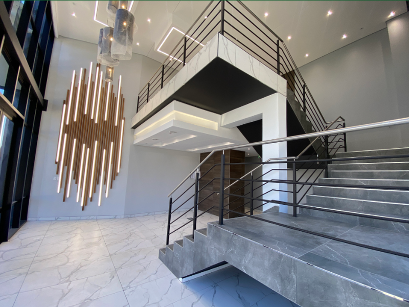 Modern industrial-style entrance foyer featuring a grand staircase, marble-look flooring, mezzanine level, and sophisticated architectural feature lighting.