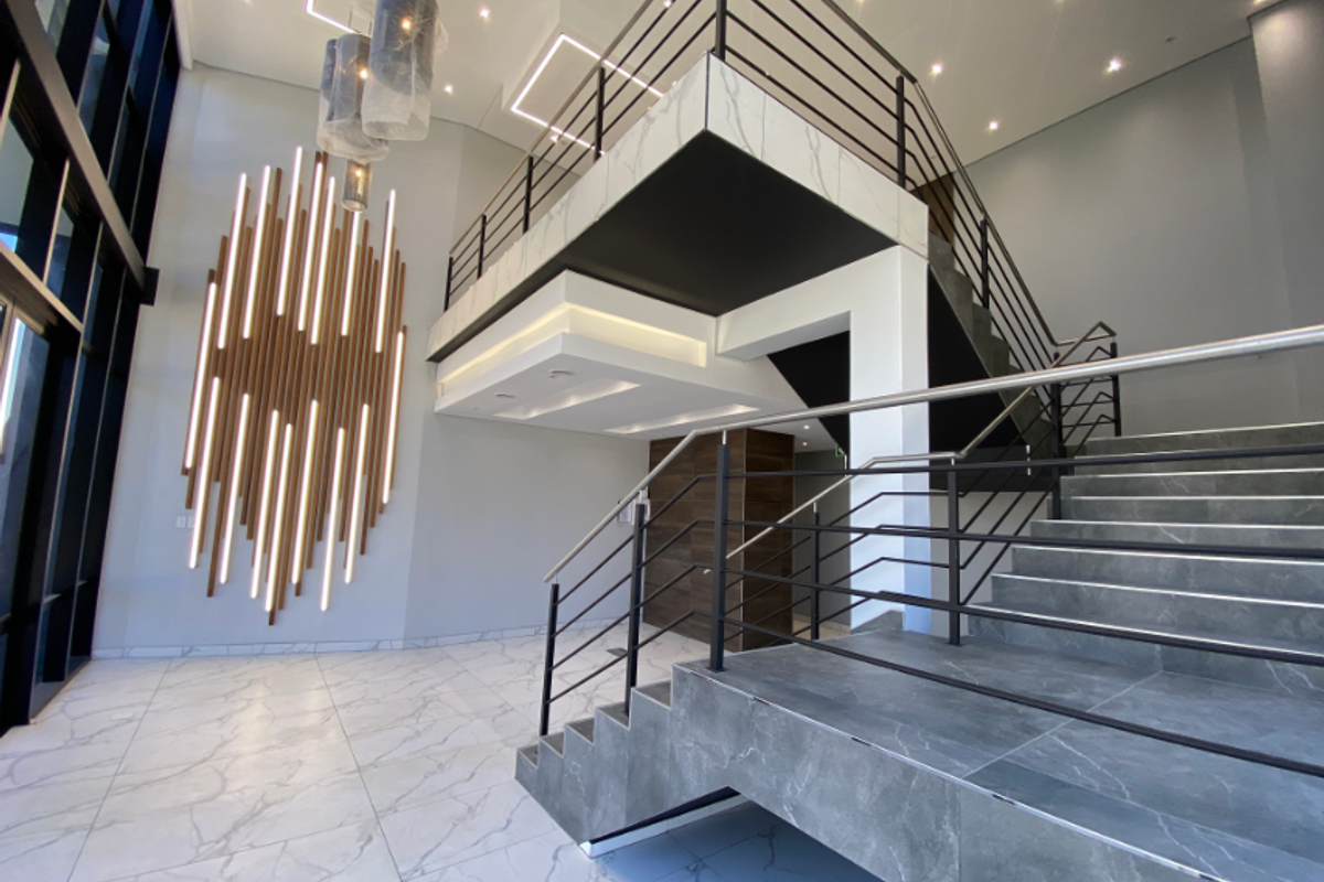 Modern industrial-style entrance foyer featuring a grand staircase, marble-look flooring, mezzanine level, and sophisticated architectural feature lighting.
