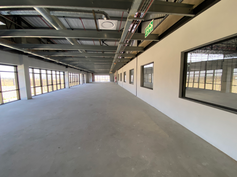 Spacious open-plan industrial unit featuring exposed steel roof trusses, polished concrete flooring, and extensive natural light through large aluminium-framed windows.