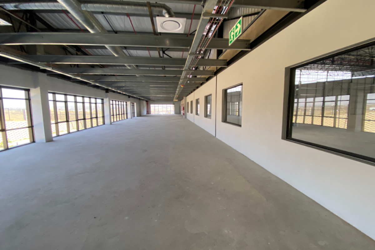 Spacious open-plan industrial unit featuring exposed steel roof trusses, polished concrete flooring, and extensive natural light through large aluminium-framed windows.