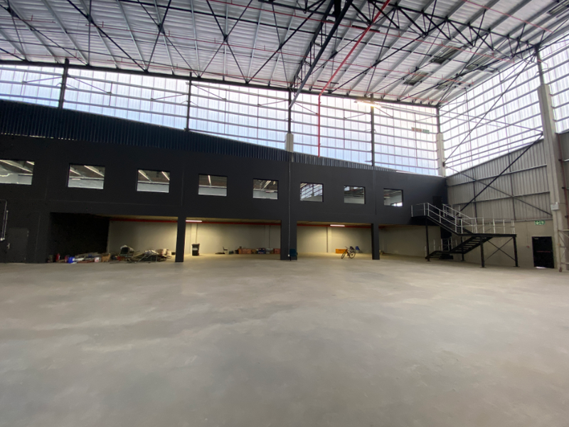 Spacious industrial warehouse featuring high ceilings, exposed steel structure, concrete flooring, and a mezzanine level with integrated staircase access.