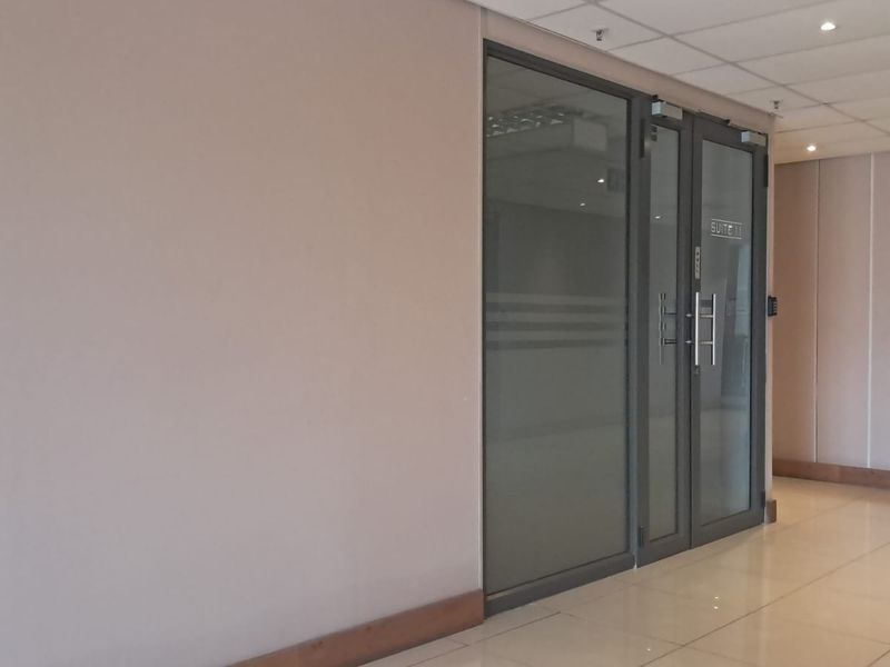 A clean, professional office suite entrance featuring glass double doors, modern tiled flooring, and a suspended ceiling with recessed lighting.