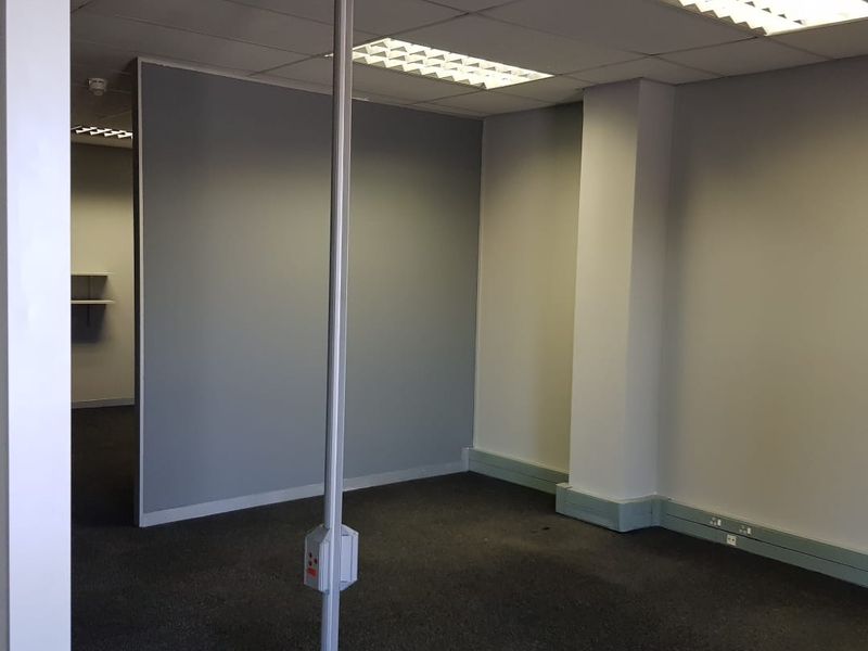 An empty office space featuring a suspended ceiling, recessed lighting, carpeted flooring, and a central power pole for workstation connectivity.