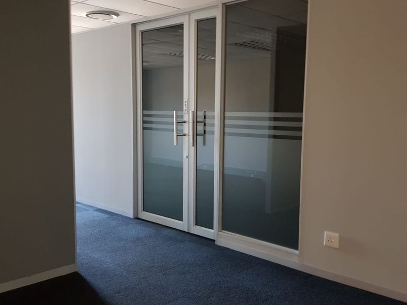 A vacant office space featuring a suspended ceiling, carpeted flooring, and modern glass partition doors with frosted detailing.