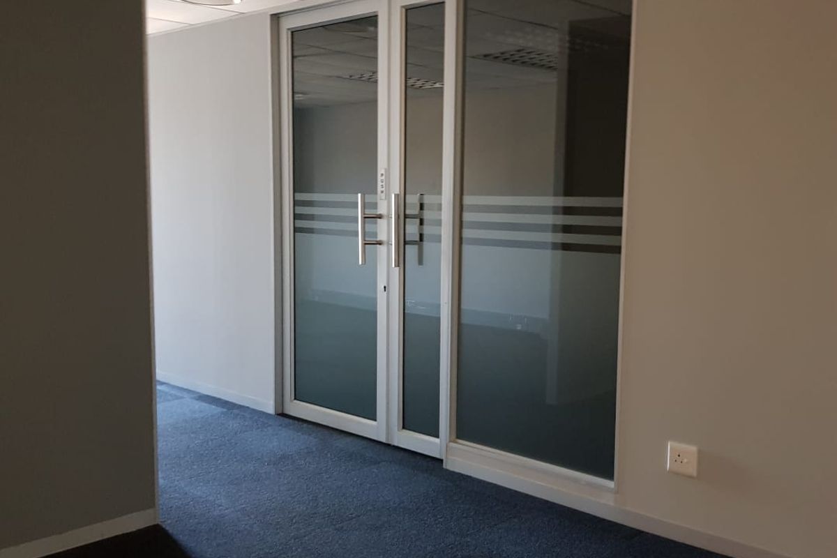 A vacant office space featuring a suspended ceiling, carpeted flooring, and modern glass partition doors with frosted detailing.