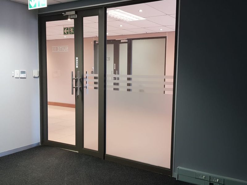 A modern office entrance featuring a glass door with frosted privacy film, suspended ceiling, and integrated electrical trunking in a professional commercial setting.
