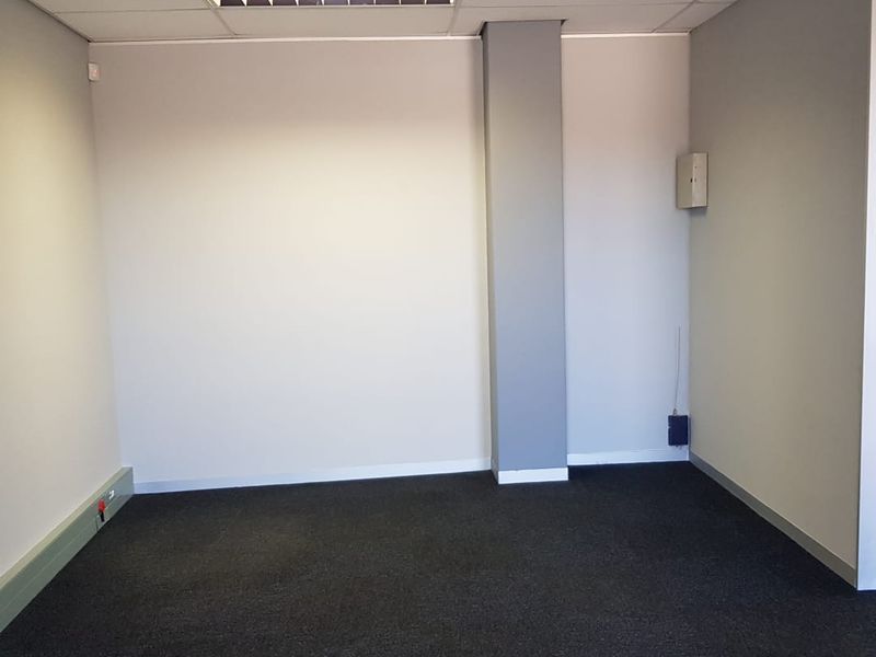 A clean, empty office space featuring neutral walls, dark carpeting, and a suspended ceiling with recessed lighting, suitable for a professional workspace.