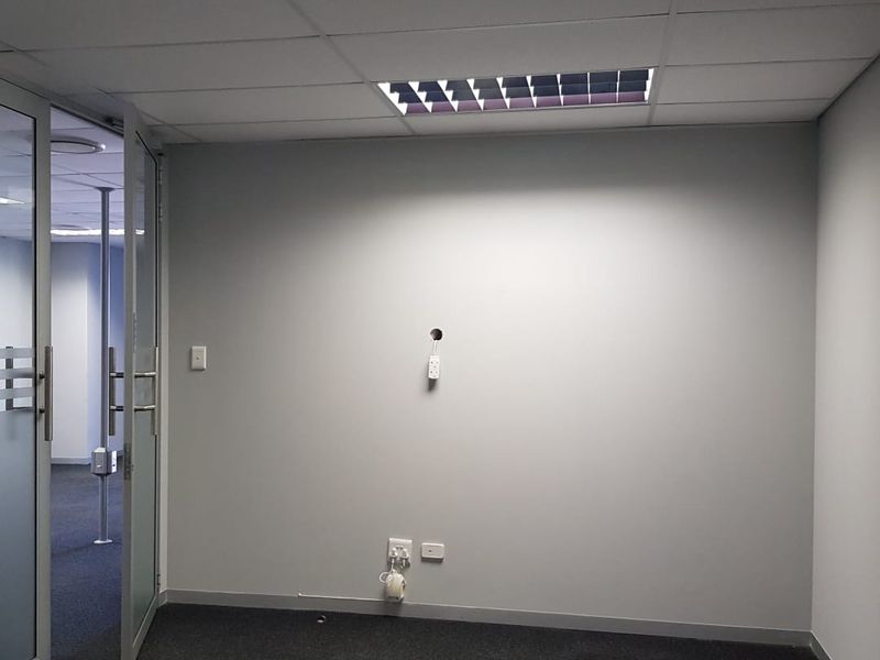 An empty office space featuring a suspended ceiling, recessed lighting, carpeted flooring, and a glass partition door, ready for professional fit-out.