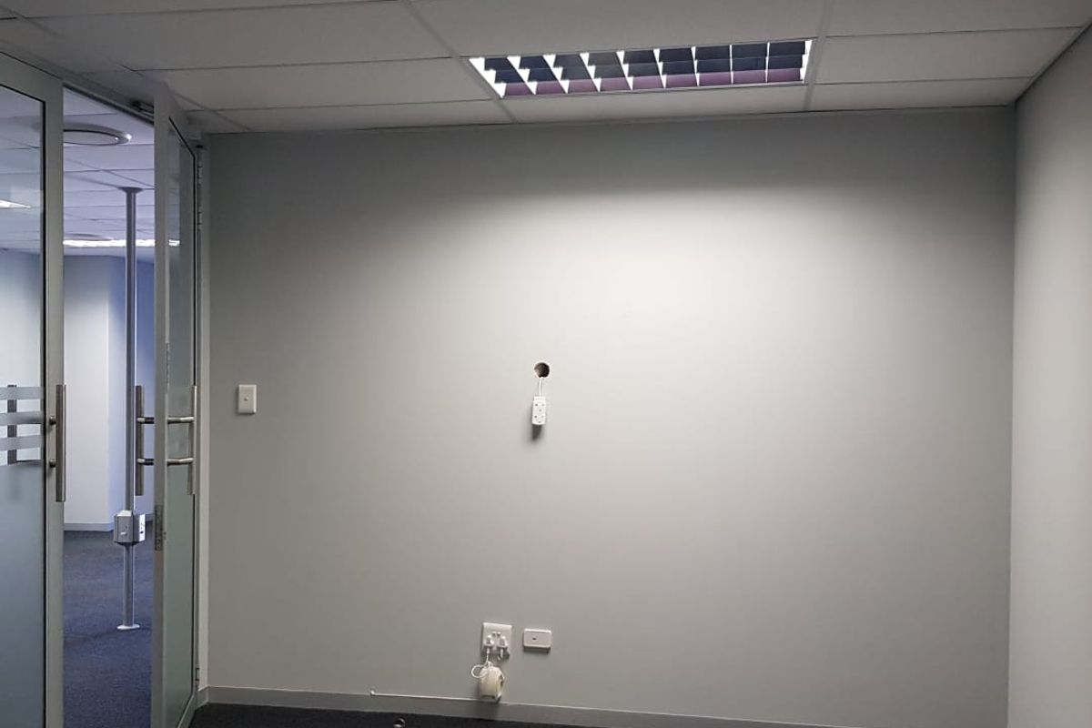 An empty office space featuring a suspended ceiling, recessed lighting, carpeted flooring, and a glass partition door, ready for professional fit-out.