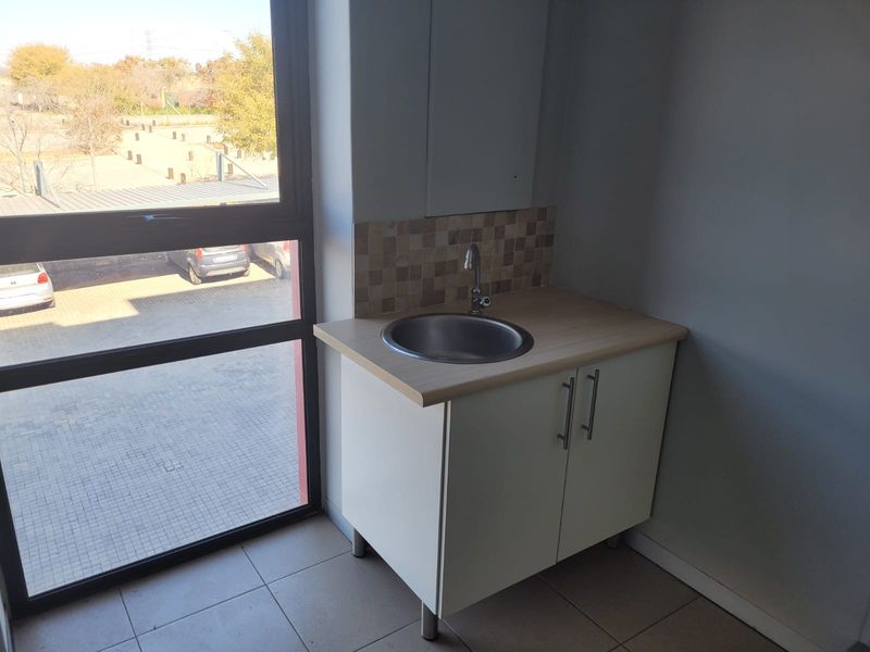 A compact kitchenette area featuring a built-in cabinet, stainless steel sink, and tiled splashback, situated next to a large window with exterior views.