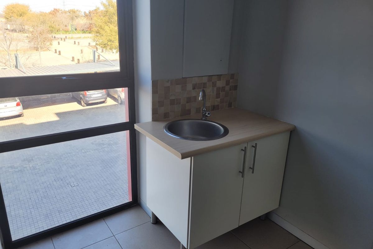 A compact kitchenette area featuring a built-in cabinet, stainless steel sink, and tiled splashback, situated next to a large window with exterior views.
