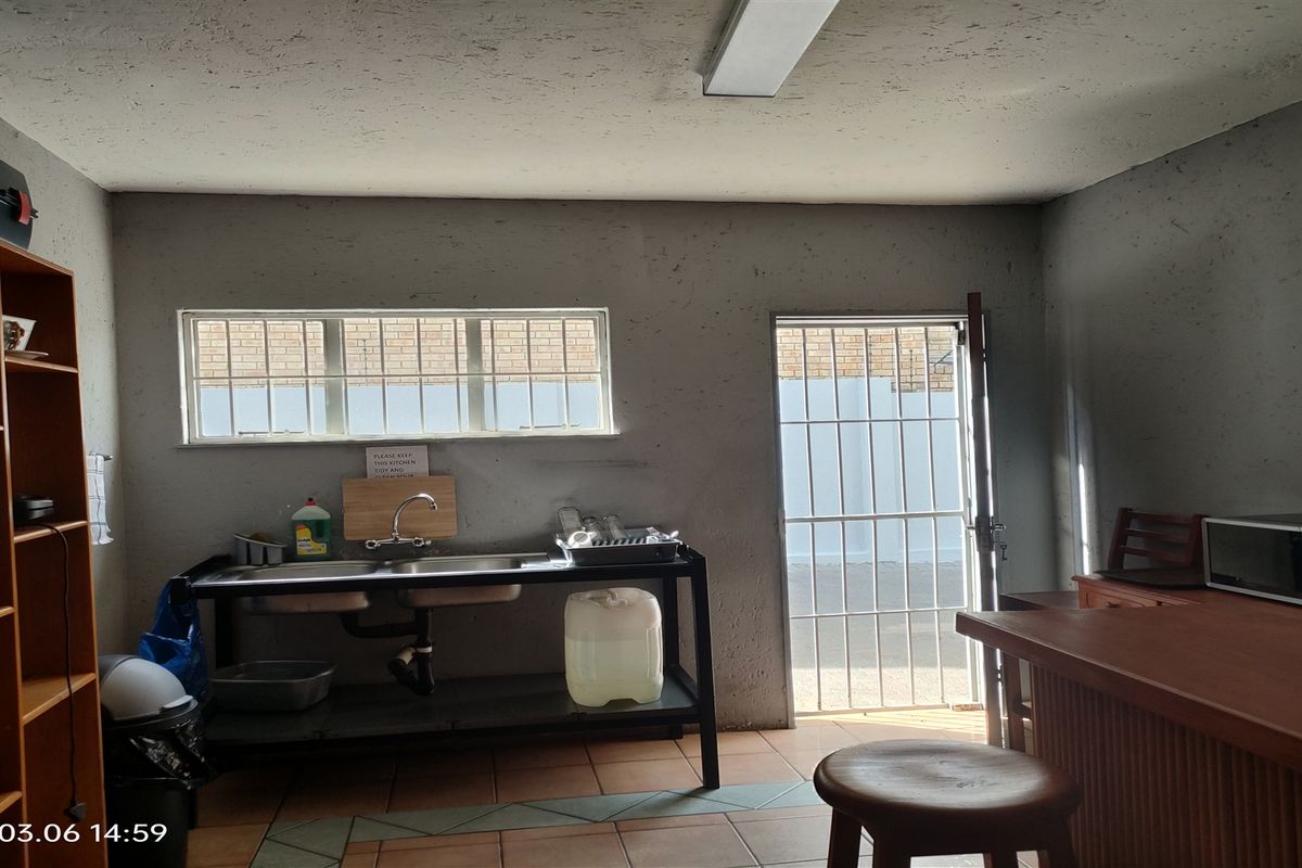 A functional industrial kitchen area featuring a stainless steel sink unit, security gate access, and basic utility space.
