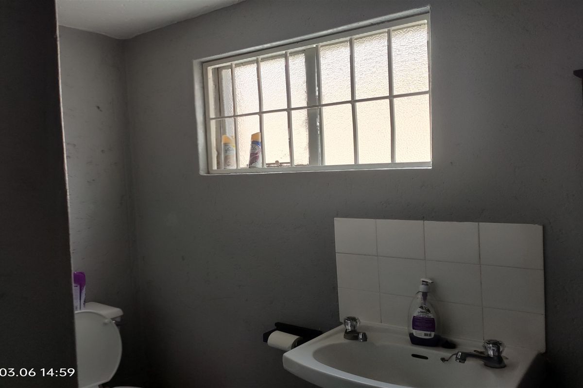 A functional bathroom featuring a wall-mounted basin with tiled splashback and a window with security bars.