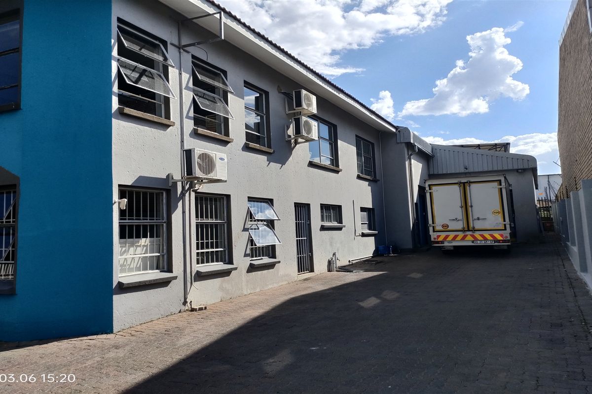 Side exterior view of the industrial property featuring paved access, multiple windows with security bars, and wall-mounted air conditioning units.