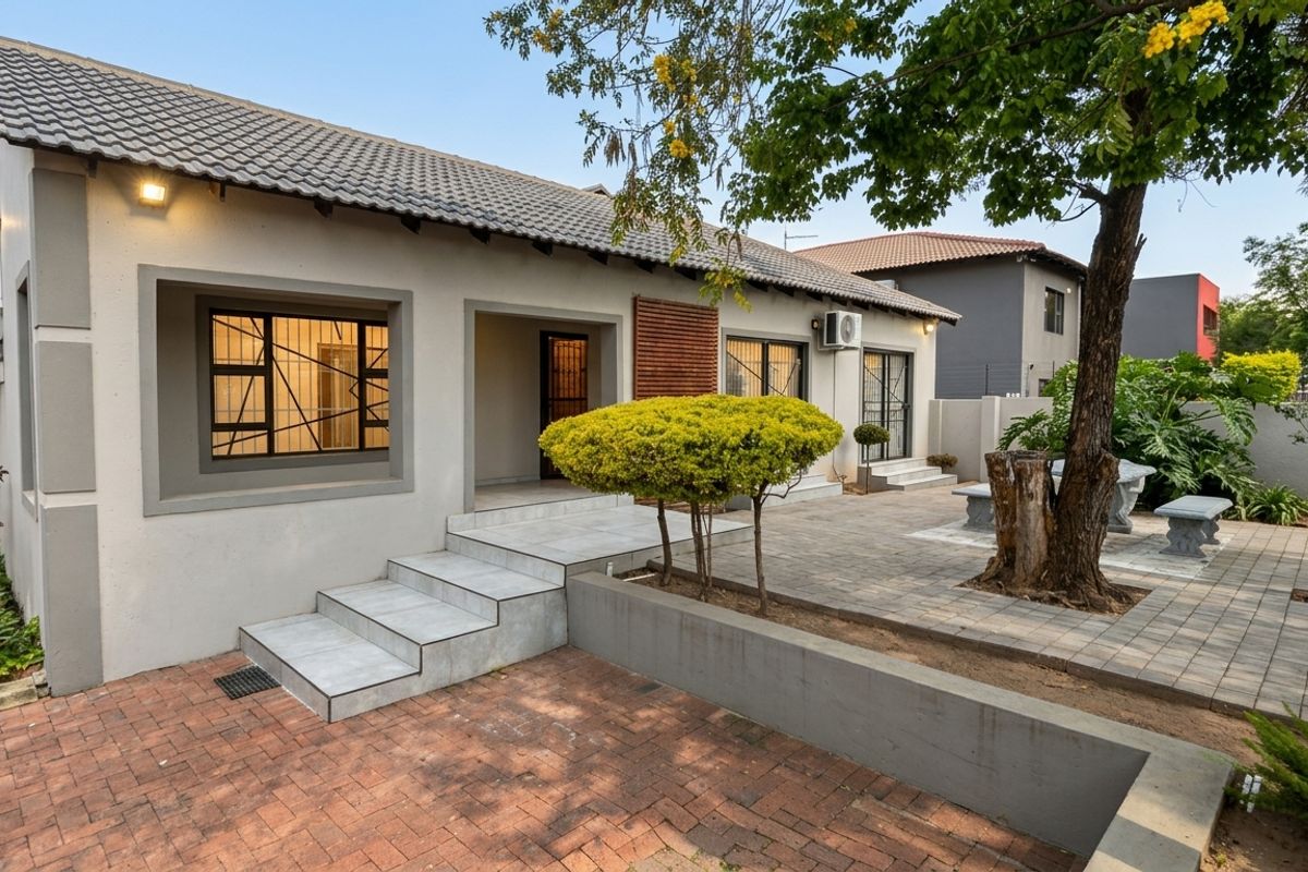 A well-maintained rear exterior view featuring a paved patio area, tiled steps, and established garden landscaping with a retaining wall.