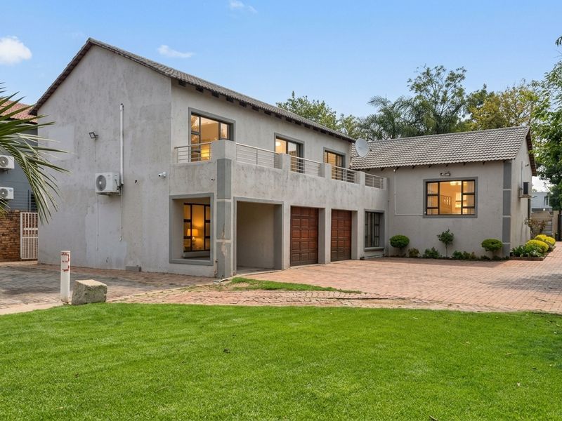 A two-story office building featuring a paved driveway, double garage, and an upper-level balcony, set within a landscaped property.