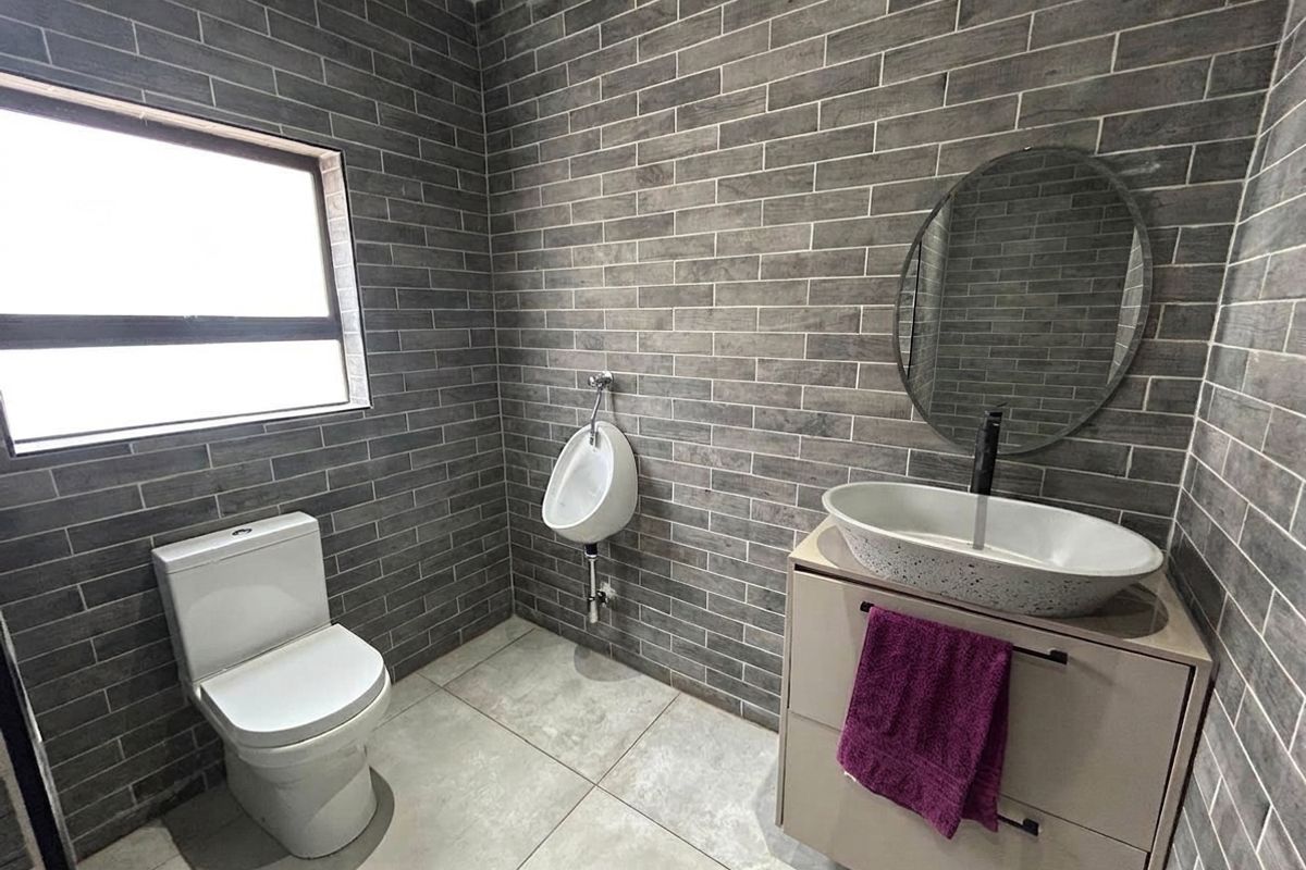 Modern office bathroom featuring grey brick-style wall tiles, a vessel sink vanity, a toilet, and a wall-mounted urinal.