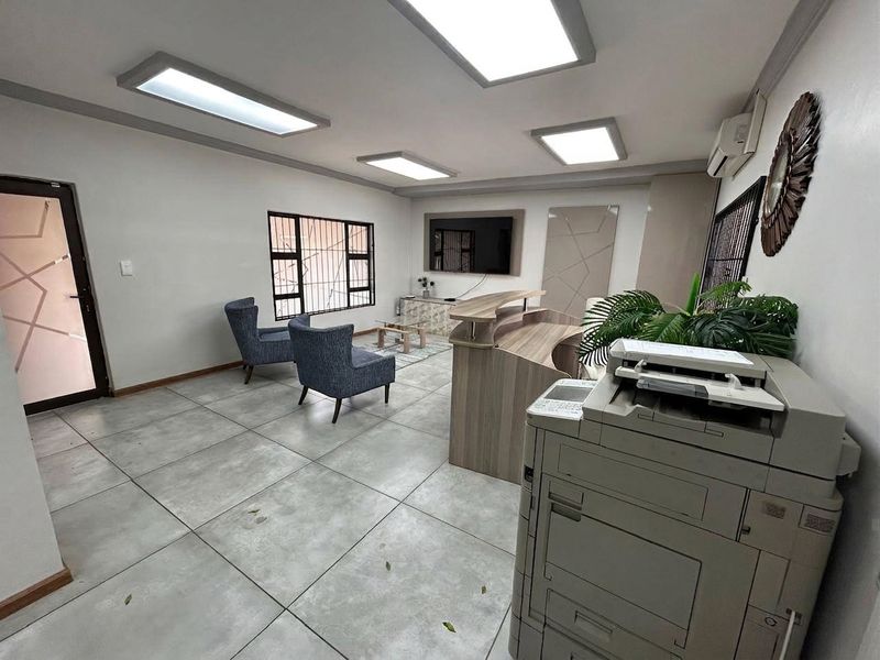 A professional office reception area featuring tiled flooring, recessed LED lighting, a built-in reception desk, and security bars on the windows.