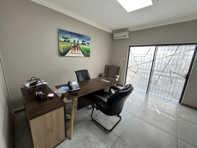 A well-maintained office space featuring tiled flooring, a wall-mounted air conditioning unit, and a large sliding glass door providing natural light.