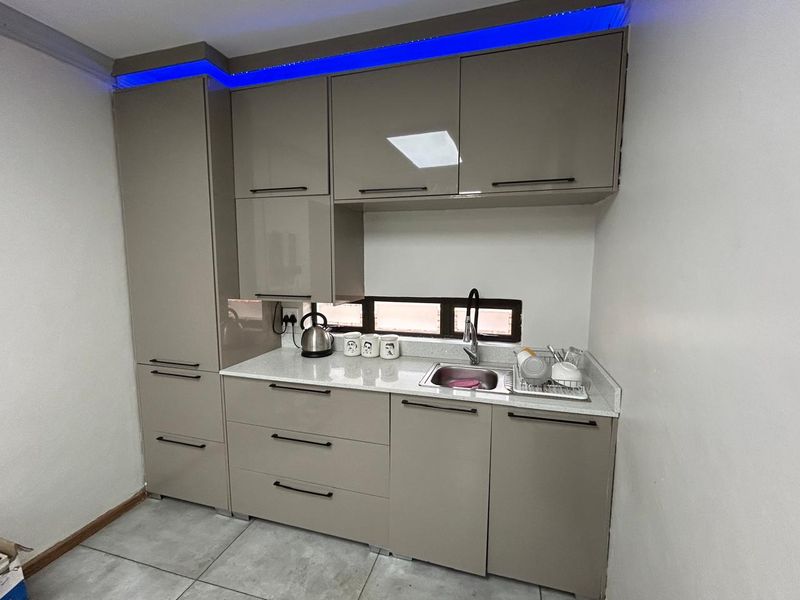 A modern, compact kitchenette featuring high-gloss cabinetry, stone countertops, a stainless steel sink, and integrated LED accent lighting.