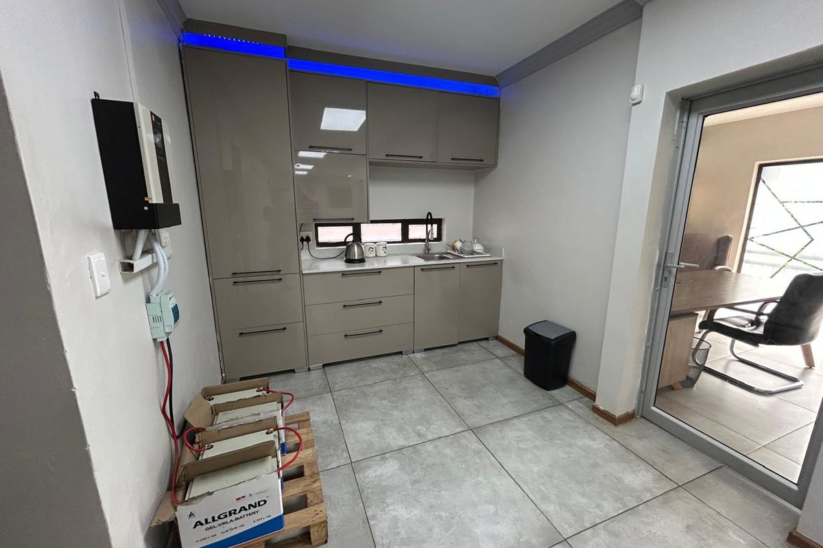 A modern kitchenette featuring sleek cabinetry, integrated LED lighting, and tiled flooring, suitable for office staff use.