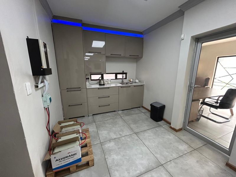 A modern kitchenette featuring sleek cabinetry, integrated LED lighting, and tiled flooring, suitable for office staff use.