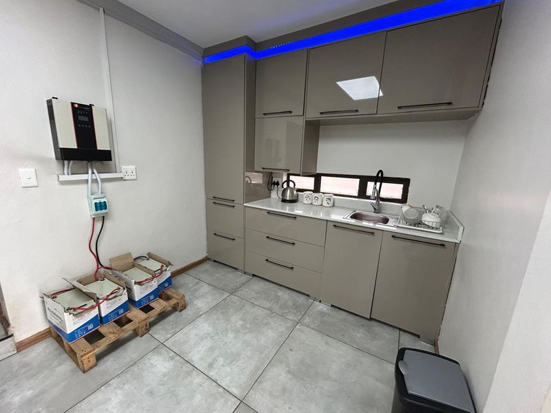 A modern kitchenette featuring high-gloss cabinetry, stone countertops, integrated sink, and a wall-mounted inverter system with battery storage.