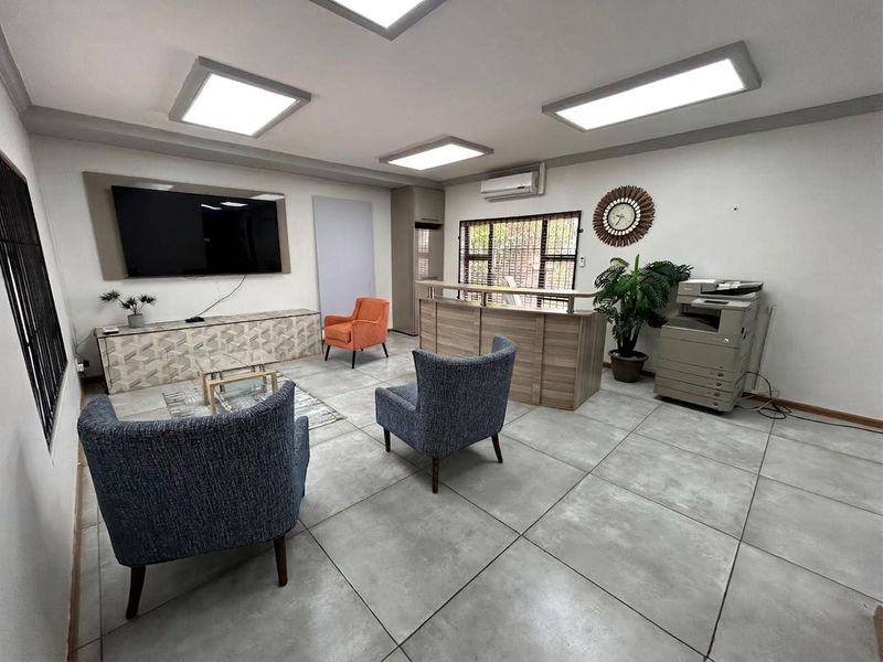 A modern office reception area featuring tiled flooring, recessed LED lighting, a built-in reception desk, and a wall-mounted air conditioning unit.