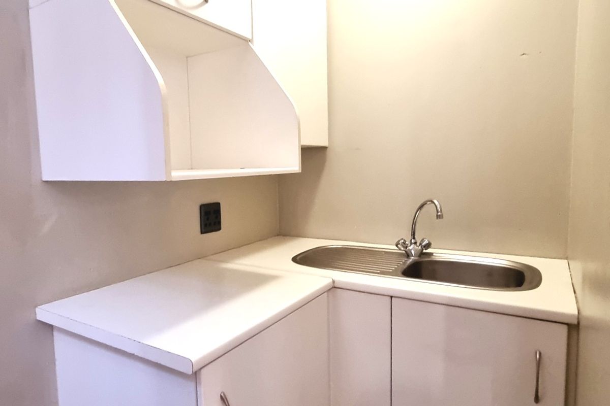 A compact kitchenette area featuring white cabinetry, a stainless steel sink with a mixer tap, and a laminate countertop.