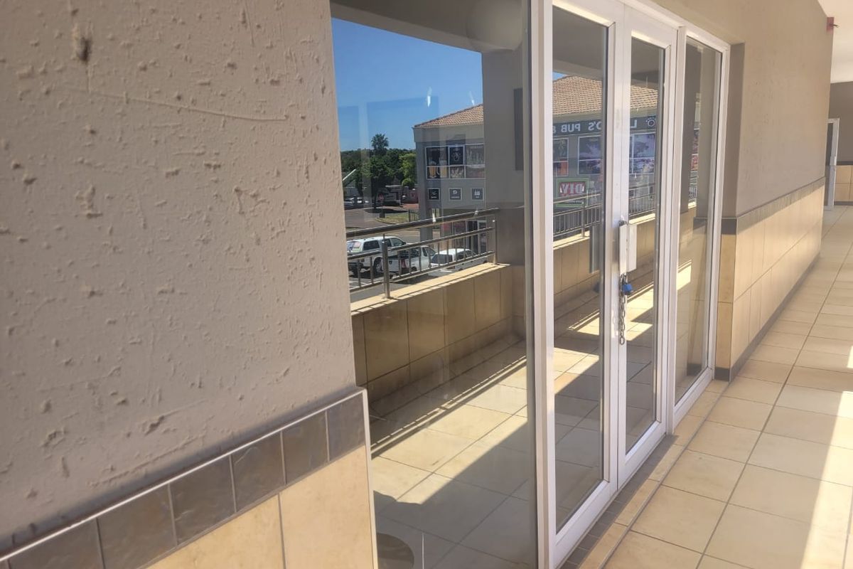 Exterior view of a retail unit featuring a tiled walkway, glass double doors, and a balcony with metal railings.