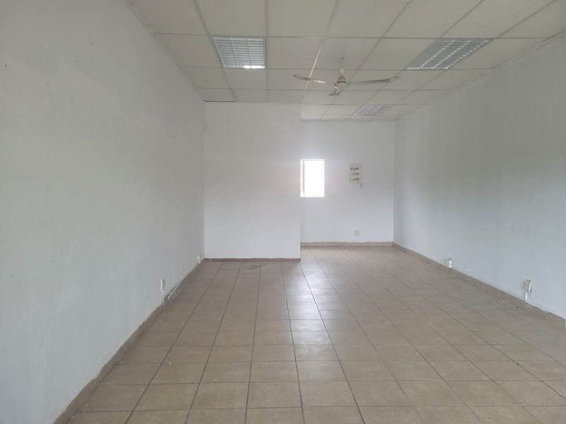 An empty, open-plan retail space featuring ceramic tiled flooring, a suspended ceiling with recessed lighting, and a ceiling fan.