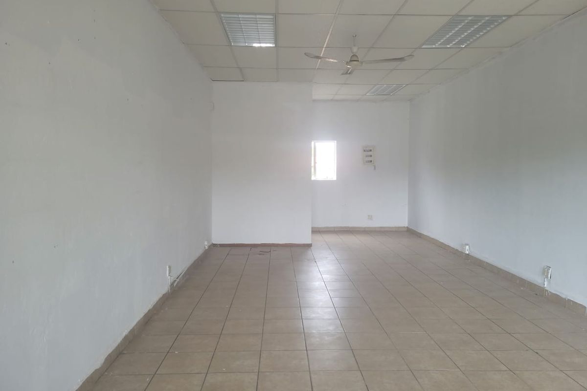 An empty, open-plan retail space featuring ceramic tiled flooring, a suspended ceiling with recessed lighting, and a ceiling fan.