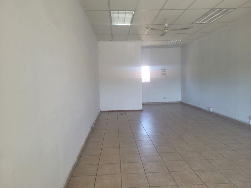 A vacant, open-plan retail space featuring ceramic tiled flooring, a suspended ceiling with recessed lighting, and a ceiling fan.