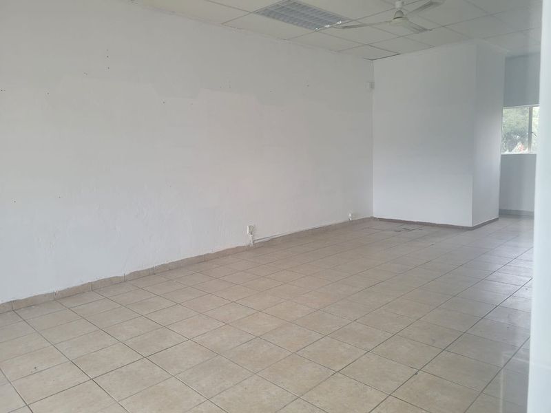 An empty, open-plan retail space featuring tiled flooring, a suspended ceiling with a fan, and neutral white walls ready for customization.