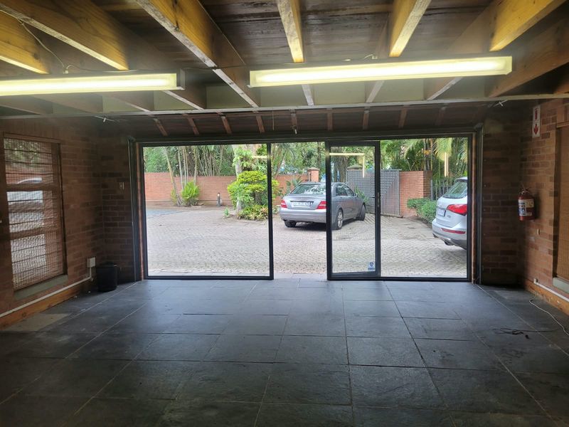 Spacious garage featuring exposed brick walls, timber ceiling beams, tiled flooring, and large sliding glass doors providing access to the paved driveway.