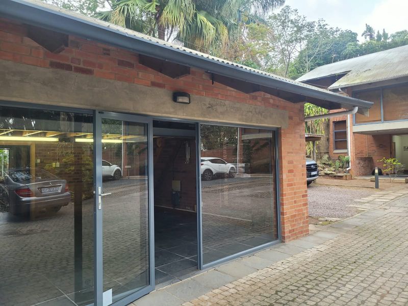 Exterior view of an office building featuring exposed brickwork, modern aluminium sliding doors, and a durable corrugated metal roof.