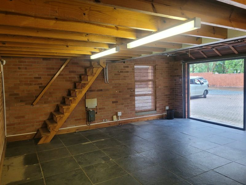 Spacious garage featuring exposed brick walls, timber ceiling beams, and a wooden staircase leading to an upper level.