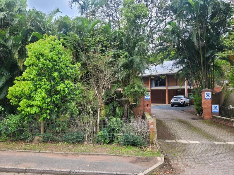 Front view of the office property featuring a brick driveway, established garden, and secure gated entrance.
